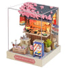 A wooden miniature dollhouse kit featuring a pink flowering roof and an interior shop display.