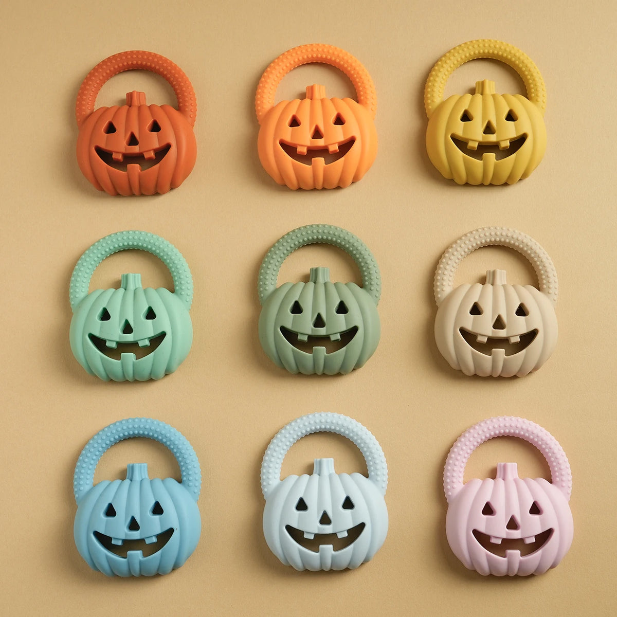 A collection of nine silicone pumpkin baby teethers in various colors including orange, yellow, mint green, beige, light blue