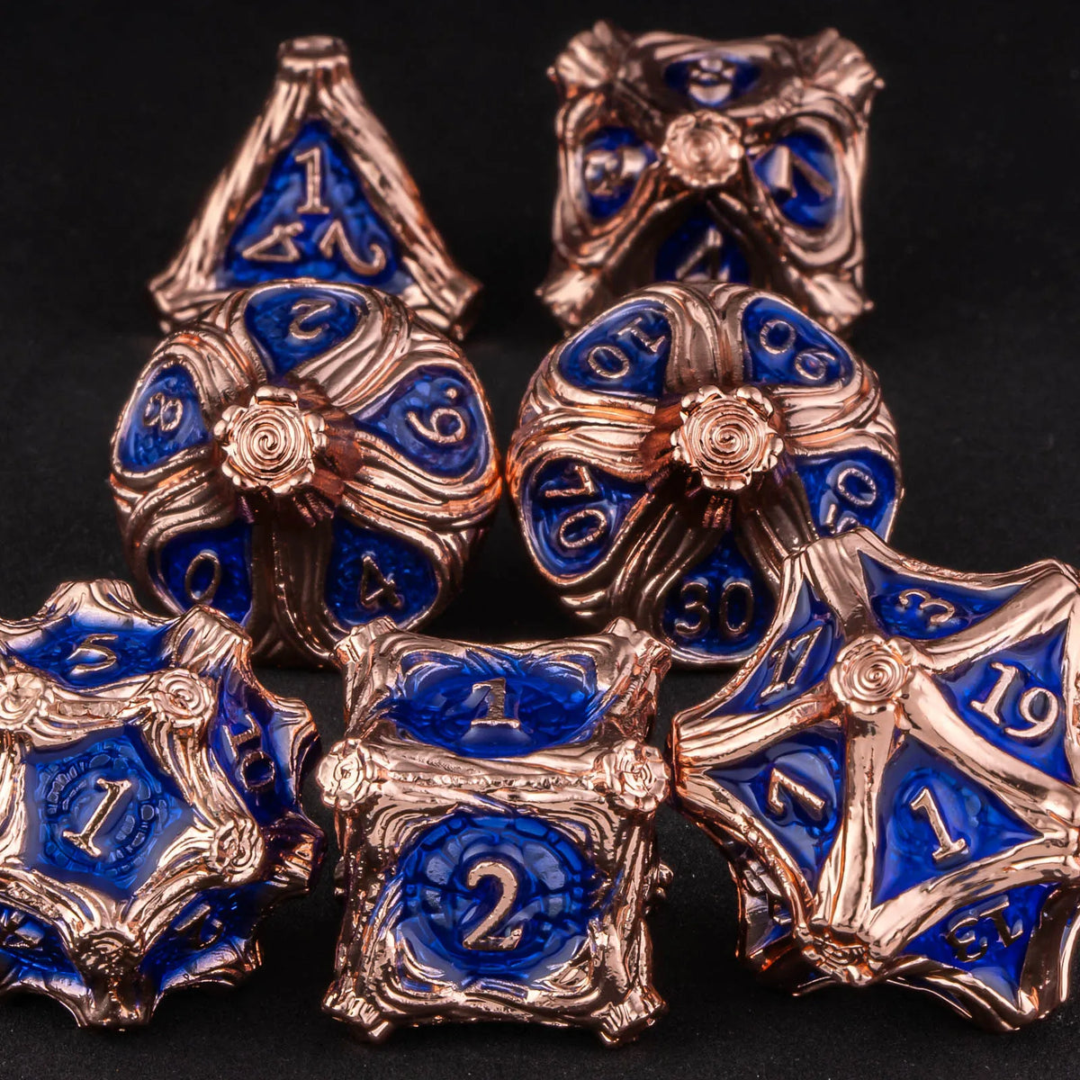 A set of seven polyhedral metal dice in gold and blue colors arranged on a dark surface.