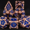 A set of seven polyhedral metal dice in gold and blue colors arranged on a dark surface.
