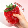 A hand holds a bright red strawberry squishy stress ball with green leaves, demonstrating its stretchy and fun texture.