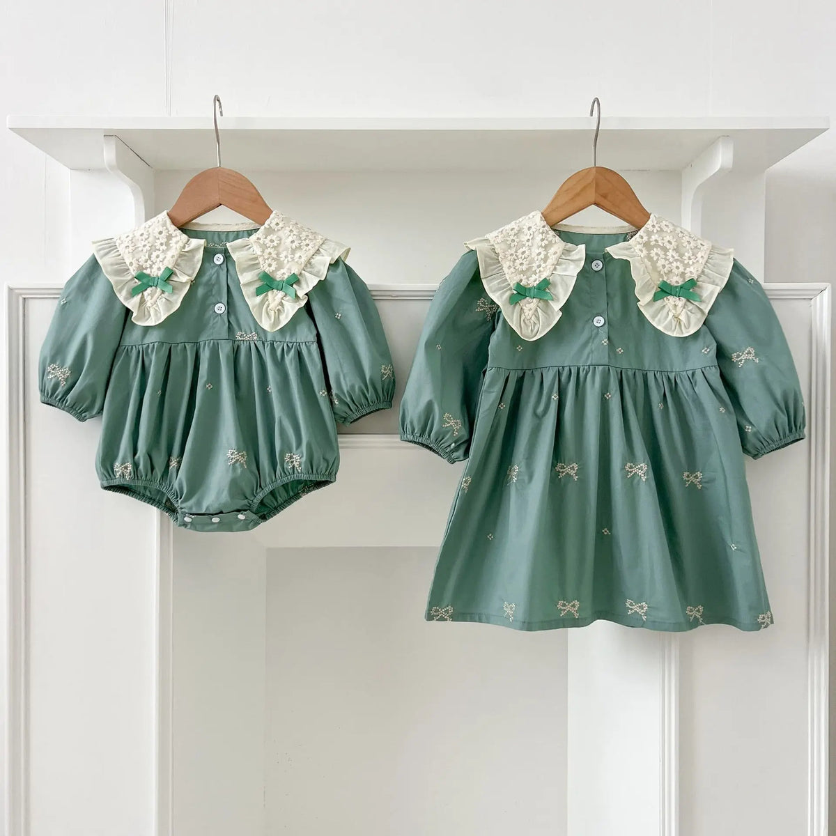 A teal cotton party dress for girls featuring white lace collar details and embroidered accents, displayed on a white shelf.