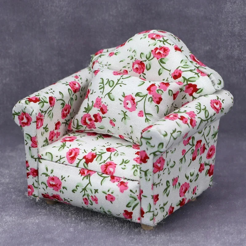 A miniature 1:12 scale sofa and pillow set for a dollhouse featuring a white fabric with pink floral patterns.