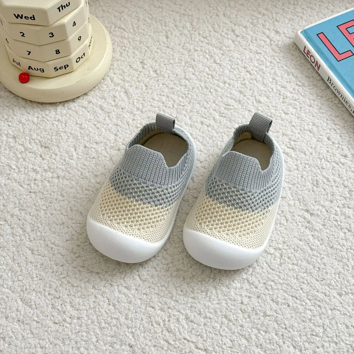 A pair of light gray and white breathable anti-slip baby first walker shoes resting on a white surface next to a calendar.