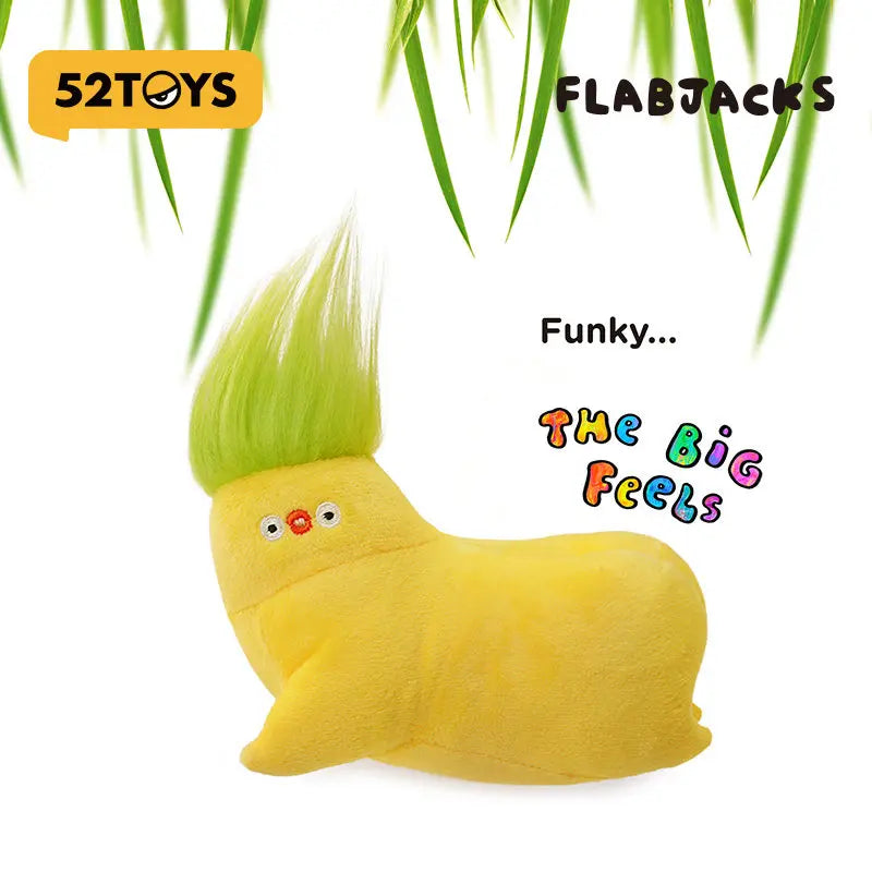 A yellow, fuzzy banana-shaped plush toy with green hair is shown against a background of green leaves.