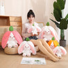 A collection of pink and white fruit bunny plush toys arranged on a wooden floor next to an open book.