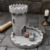 A gray medieval castle dice tower with a tray holding several polyhedral dice on a stone surface.