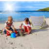 Two children play in the sand with an instant pop-up baby tent nearby on a sunny beach.