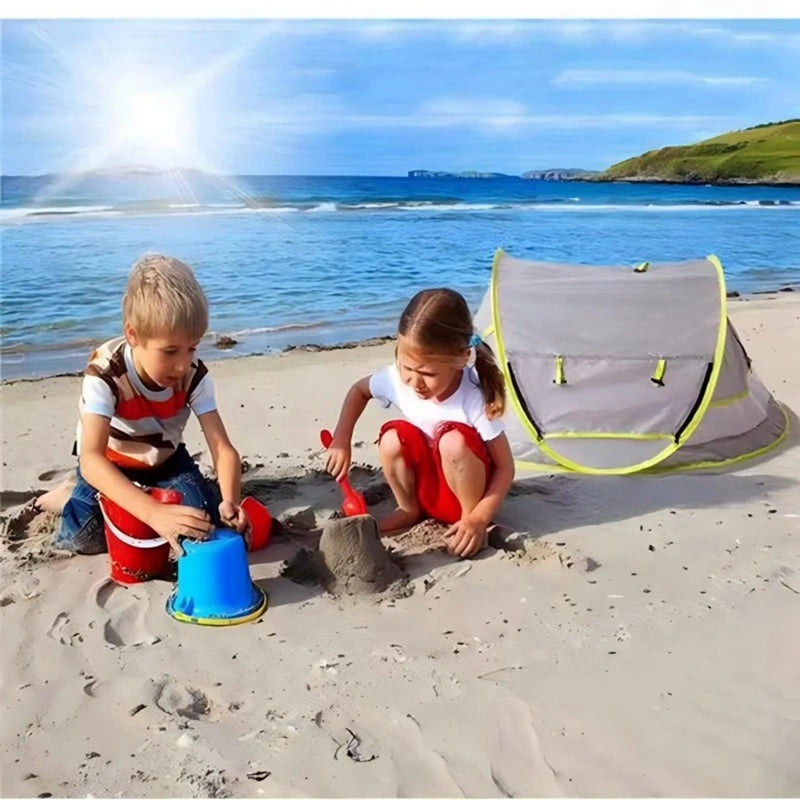 Two children play in the sand with an instant pop-up baby tent nearby on a sunny beach.