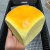A yellow and orange squishy toy shaped like a slice of fruit is held in a hand inside a black mesh basket.