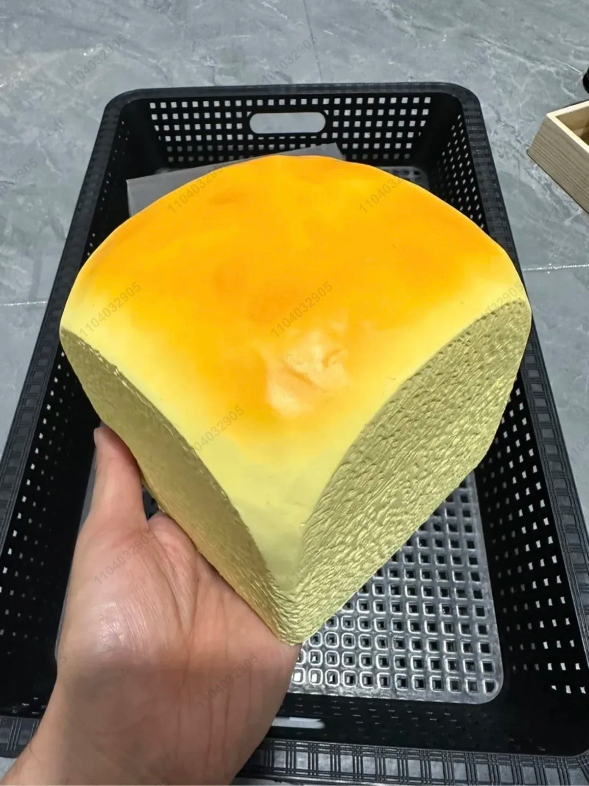 A yellow and orange squishy toy shaped like a slice of fruit is held in a hand inside a black mesh basket.
