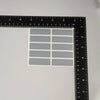 A sheet of gray scratch-off stickers is shown next to a ruler for scale.