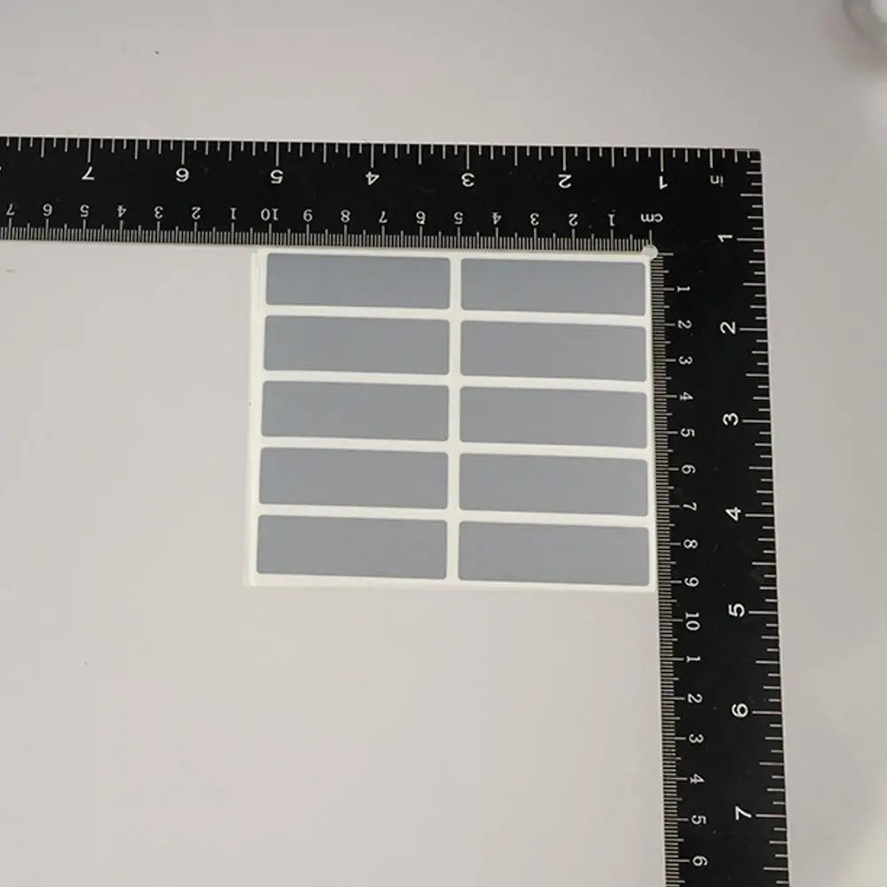 A sheet of gray scratch-off stickers is shown next to a ruler for scale.