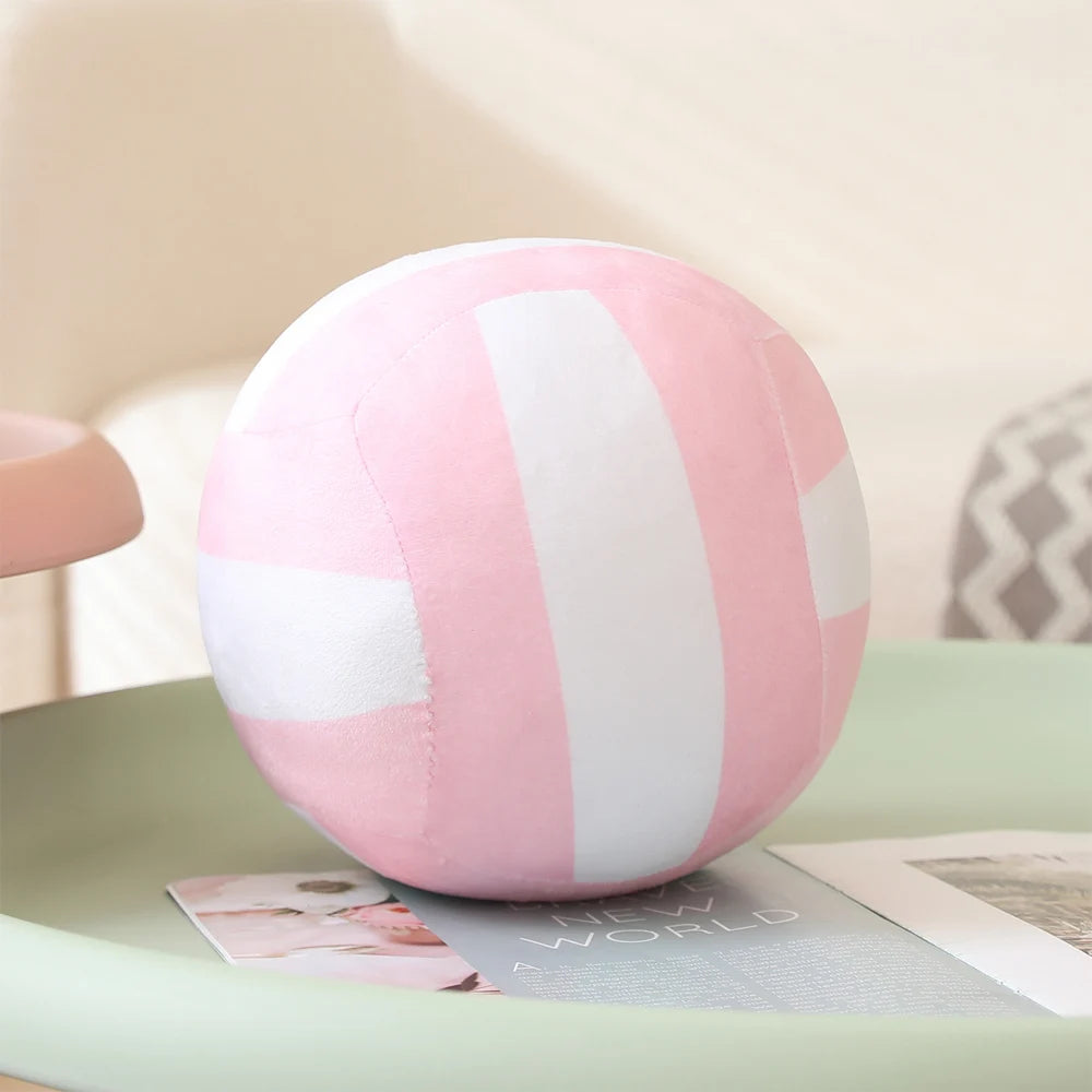 Pink and white striped soft plush volleyball pillow resting on a light green surface.