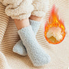 A pair of light blue fleece socks resting on a beige knitted fabric next to a small flame.