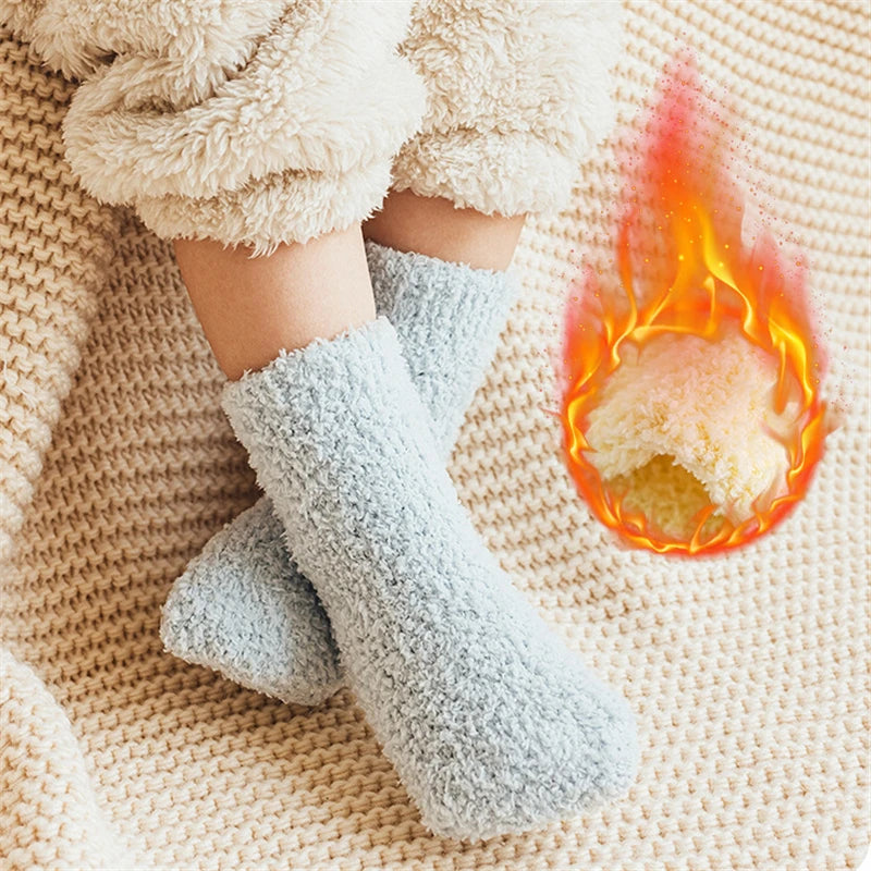 A pair of light blue fleece socks resting on a beige knitted fabric next to a small flame.