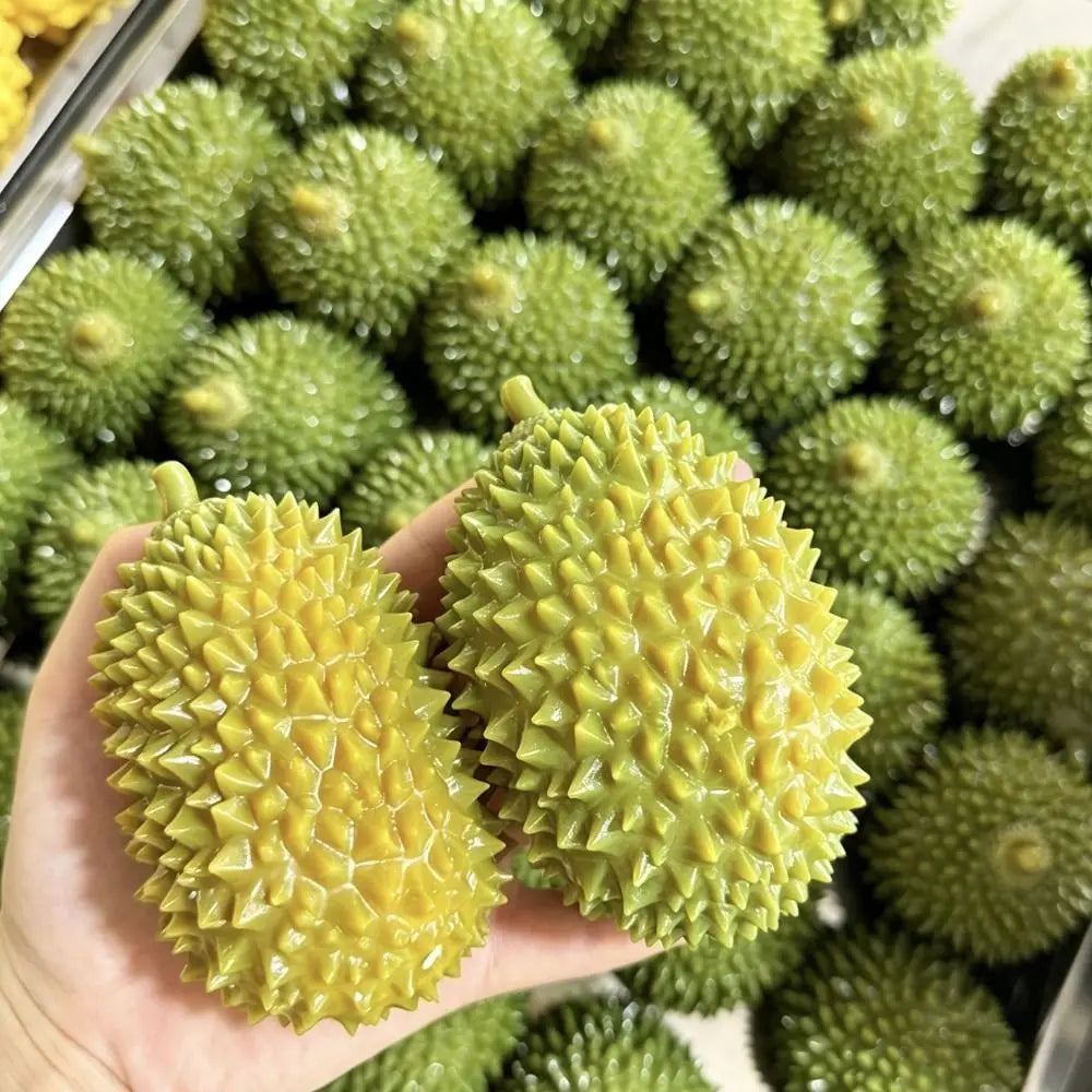 A hand holds a bright green crunchy durian squeeze toy with a textured surface.