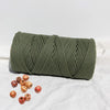 A coil of natural cotton macrame rope in olive green resting on a white surface with small wooden beads.