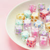 A collection of colorful floral square resin beads in various shades of pink, purple, and green arranged on a white plate.