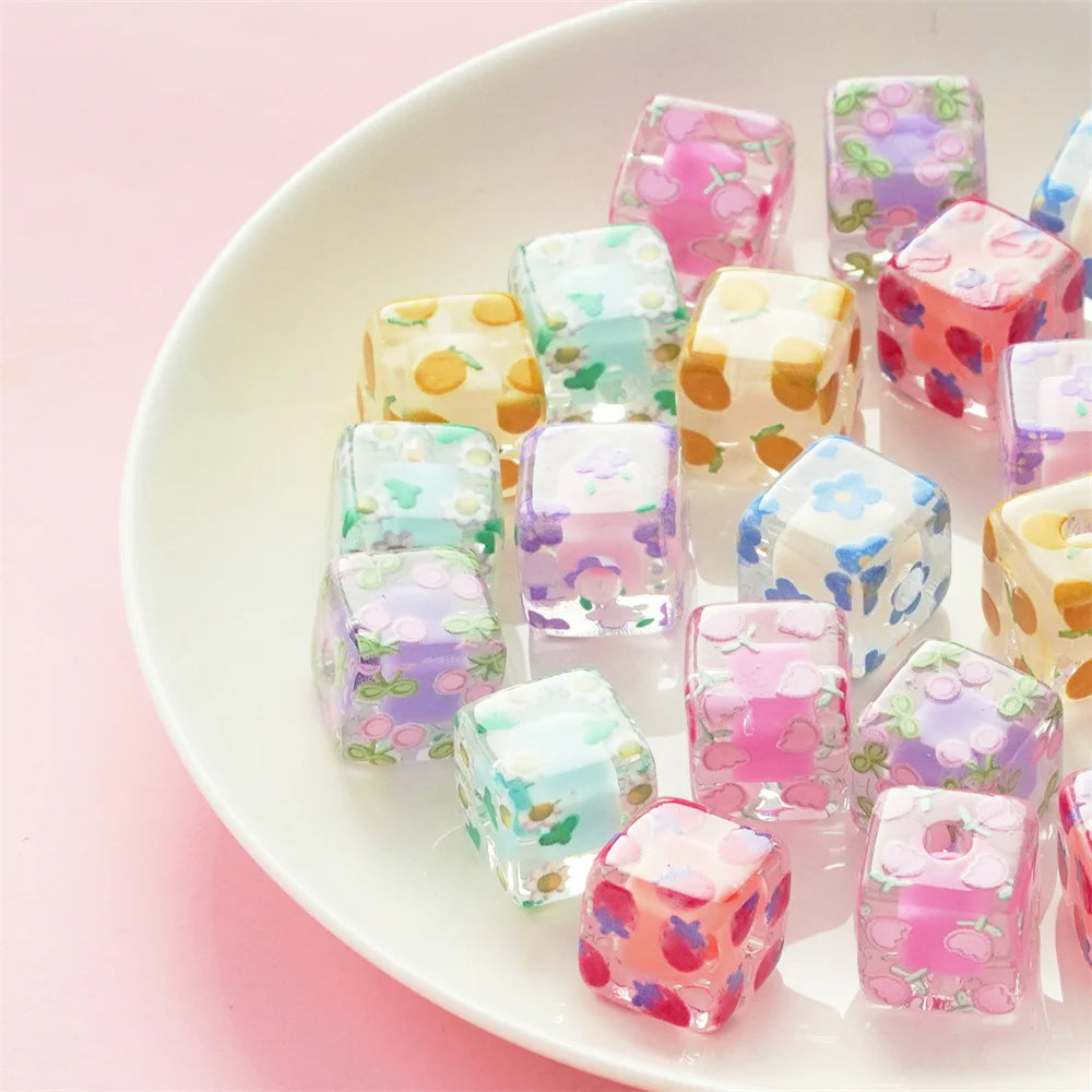 A collection of colorful floral square resin beads in various shades of pink, purple, and green arranged on a white plate.