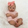 A realistic reborn baby doll with light skin, blue eyes, and pink clothing, resting in white fluffy fabric.