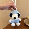 A light blue Snoopy plush charm wearing a hat is being held by a hand, ready to be attached to a bag.