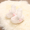 Pair of soft, white cartoon baby booties with pink ears resting on a fluffy white rug.