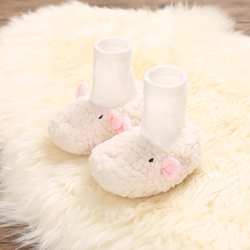 Pair of soft, white cartoon baby booties with pink ears resting on a fluffy white rug.