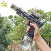 A hand holds an electric pulse water gun with a simulated flame effect against a blurred outdoor background.