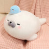 A white seal plush toy wearing a light blue octopus hat, resting on pink fabric.
