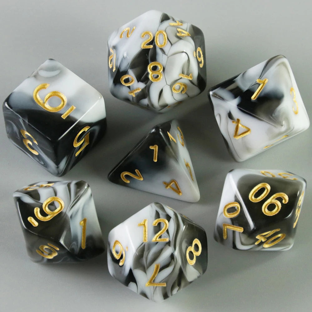 A set of black and white acrylic dice with gold numbering, displayed on a gray surface.