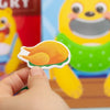 A hand is holding a wooden bear feeding game piece shaped like an orange slice for fine motor skill practice.