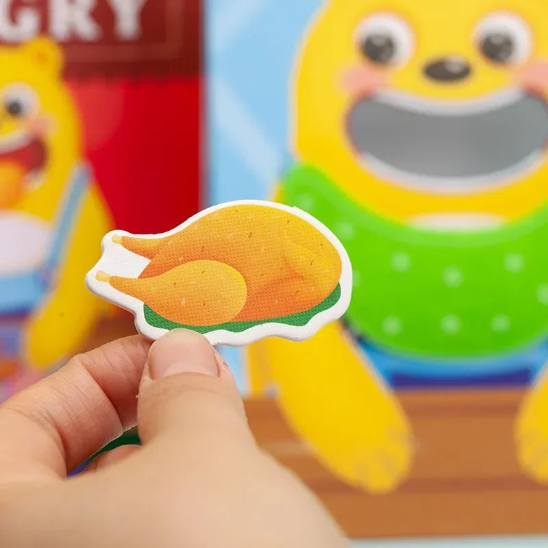 A hand is holding a wooden bear feeding game piece shaped like an orange slice for fine motor skill practice.