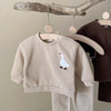 A beige baby long sleeve cartoon top and pants set displayed on a wooden hanger.