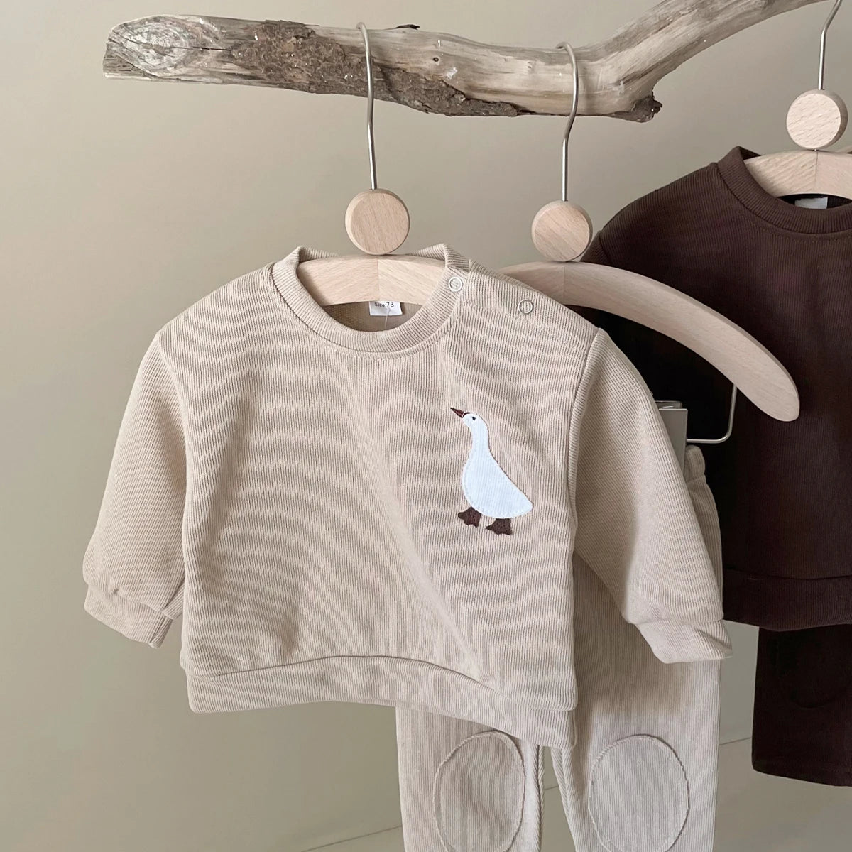 A beige baby long sleeve cartoon top and pants set displayed on a wooden hanger.