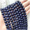 A hand holds a strand of dark blue iridescent beads for DIY jewelry making