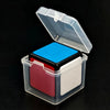 A clear plastic box with an open lid containing a blue cube and a red piece.
