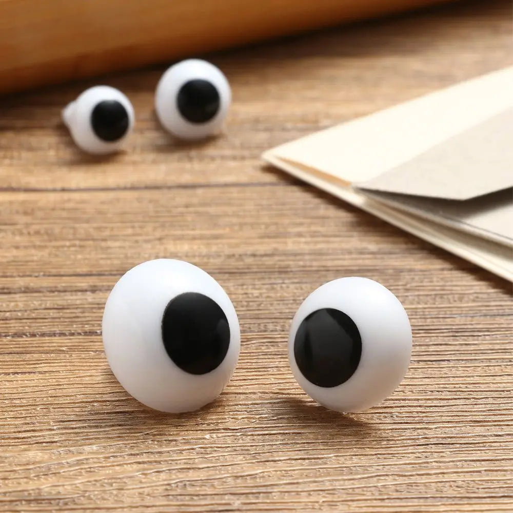 Two plastic safety eyes with white and black irises resting on a wooden surface.