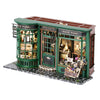 A miniature dollhouse shop set featuring a green wooden building with glass windows and various items.