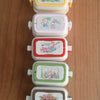 A stack of five miniature doll picnic lunch boxes in pastel colors with handles.