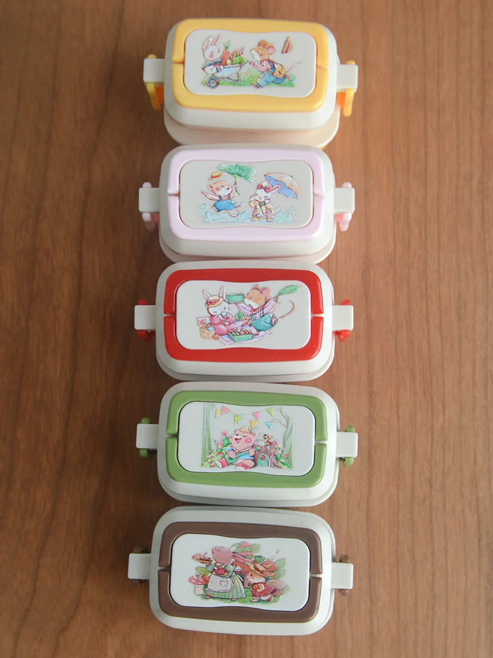 A stack of five miniature doll picnic lunch boxes in pastel colors with handles.