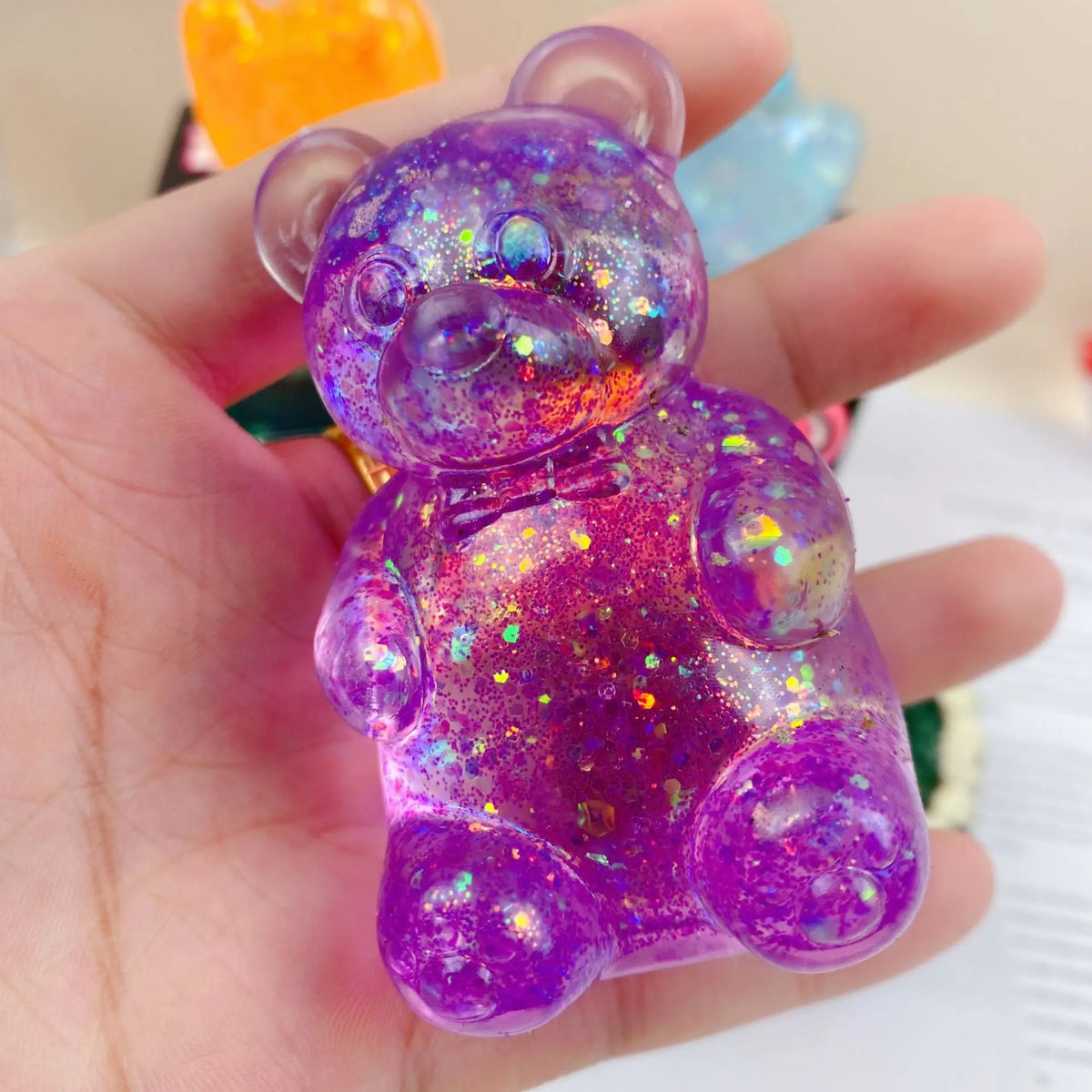 A hand holds a purple glitter bear squishy toy for stress relief.