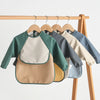 A display of various waterproof long-sleeved baby bibs hanging on a wooden rack.
