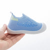 A hand holds a light blue breathable mesh slip-on sneaker for toddlers.