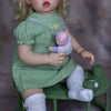 A realistic reborn baby doll with soft cloth body wearing a green dress and white socks.