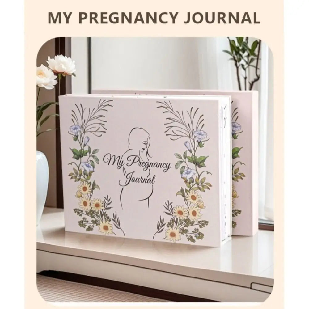 A pink pregnancy journal with floral and silhouette designs is displayed on a white surface.