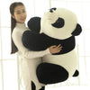 A woman is hugging a large white and black panda plush pillow in a bright, indoor setting.