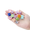A hand holds various colorful butterfly shell acrylic beads in shades of pink, purple, green, and blue.