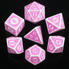 A set of pink polyhedral dice showing various numbers and geometric shapes on a black reflective surface.