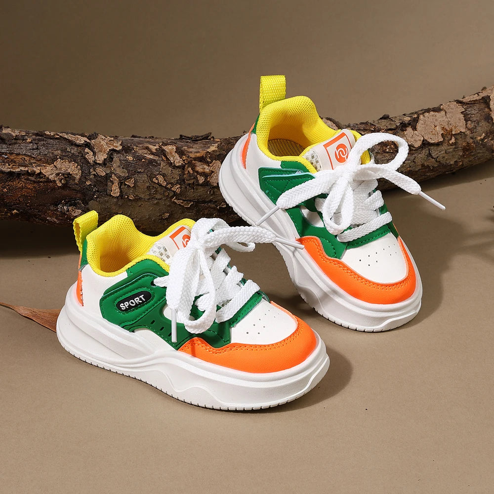 A pair of yellow and green casual sneakers with white laces and orange accents resting on a brown log.